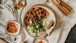 A bowl of creamy cashew pasta with vibrant spinach, twirled on a fork, on a white tablecloth. A jar of nutritional yeast and a lemon wedge sit on a rustic wooden table, with a cozy kitchen backdrop.